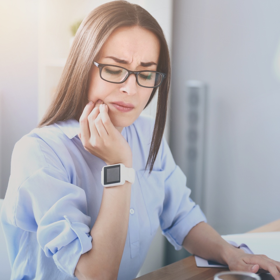 Unbearable toothache. Good looking bespectacled woman working on laptop and having toothache while sitting by the table.