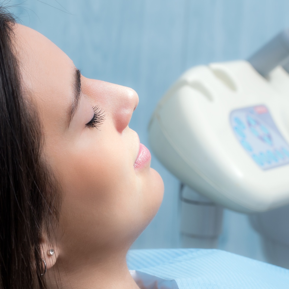 Close up side view portrait of young woman at dental check up.Girl laying with eyes closed with equipment in background.