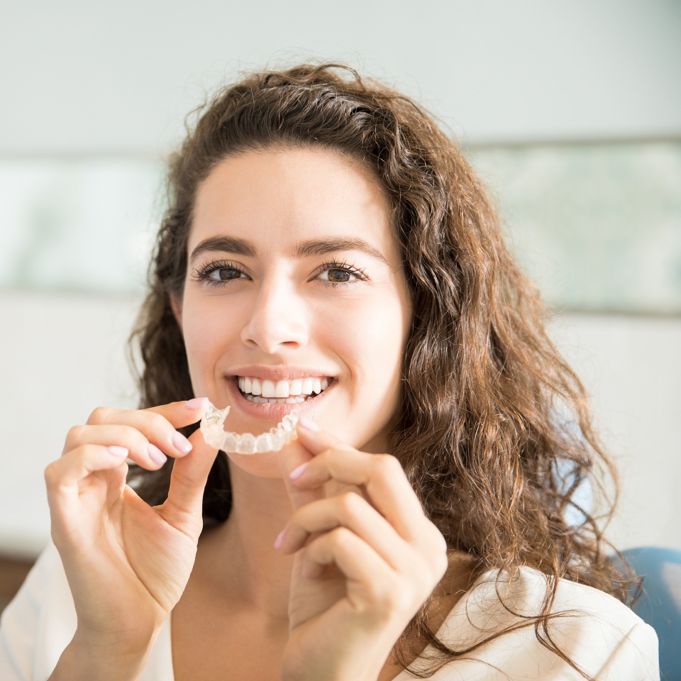 Portrait of beautiful patient holding orthodontic retainers in dental clinic