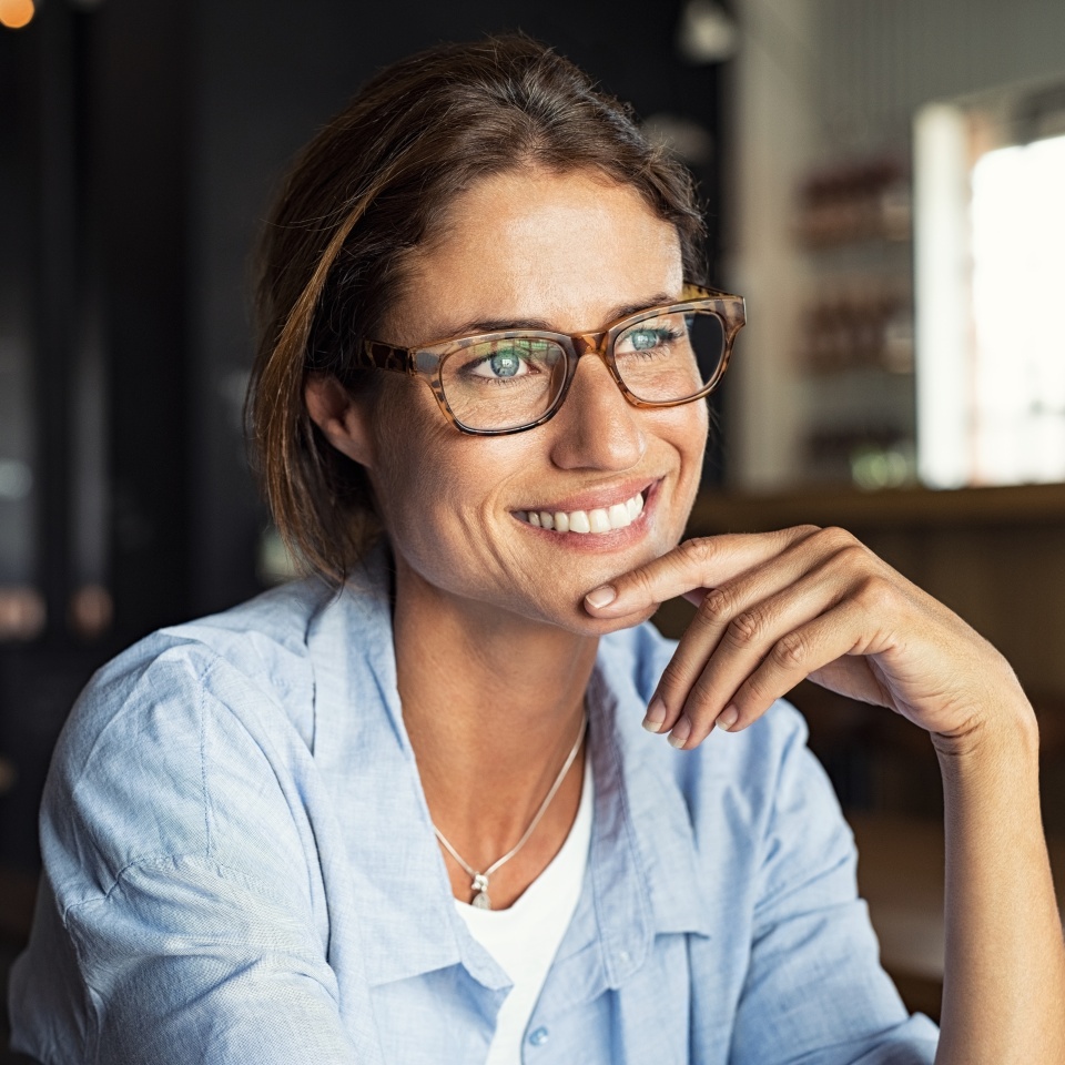 Portrait of beautiful mature woman sitting in cafeteria looking away. Cheerful mature woman wearing eyeglasses thinking with finger on chin. Happy woman relaxing at cafe and smiling.