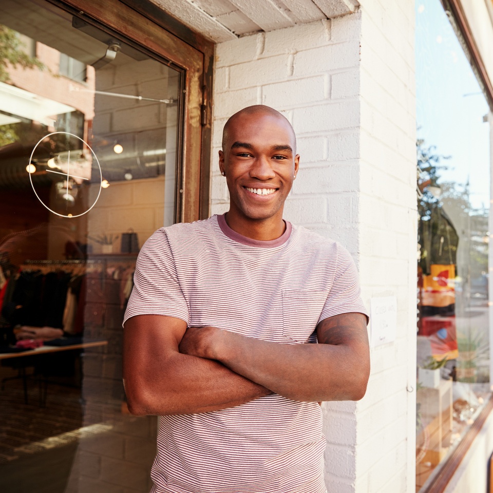 Young black man smiling to camera outside his clothes shop