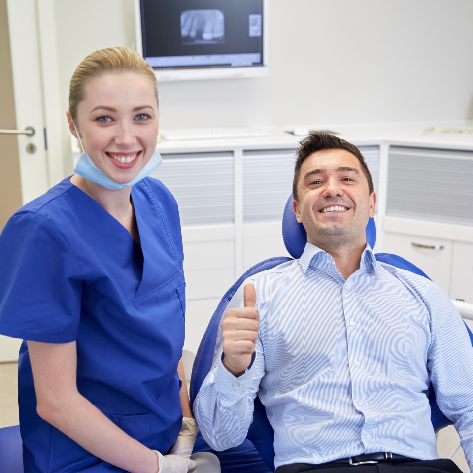 people, medicine, stomatology, gesture and health care concept - happy female dentist with man patient showing thumbs up at dental clinic office