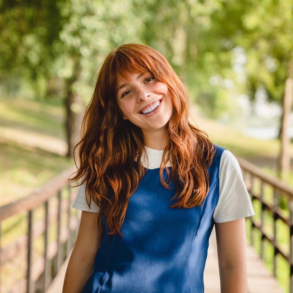Good-looking caucasian teenage girl young woman student walking outdoors in park, looking at camera. Schoolgirl with red ginger hair relaxing in forest.