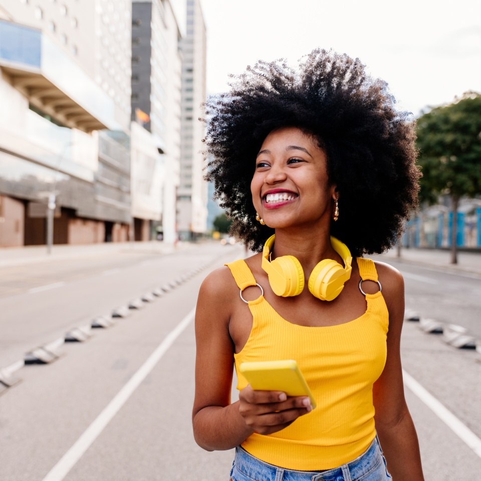 Beautiful young happy african woman with afro curly hairstyle strolling in the city - Cheerful black student walking on the streets