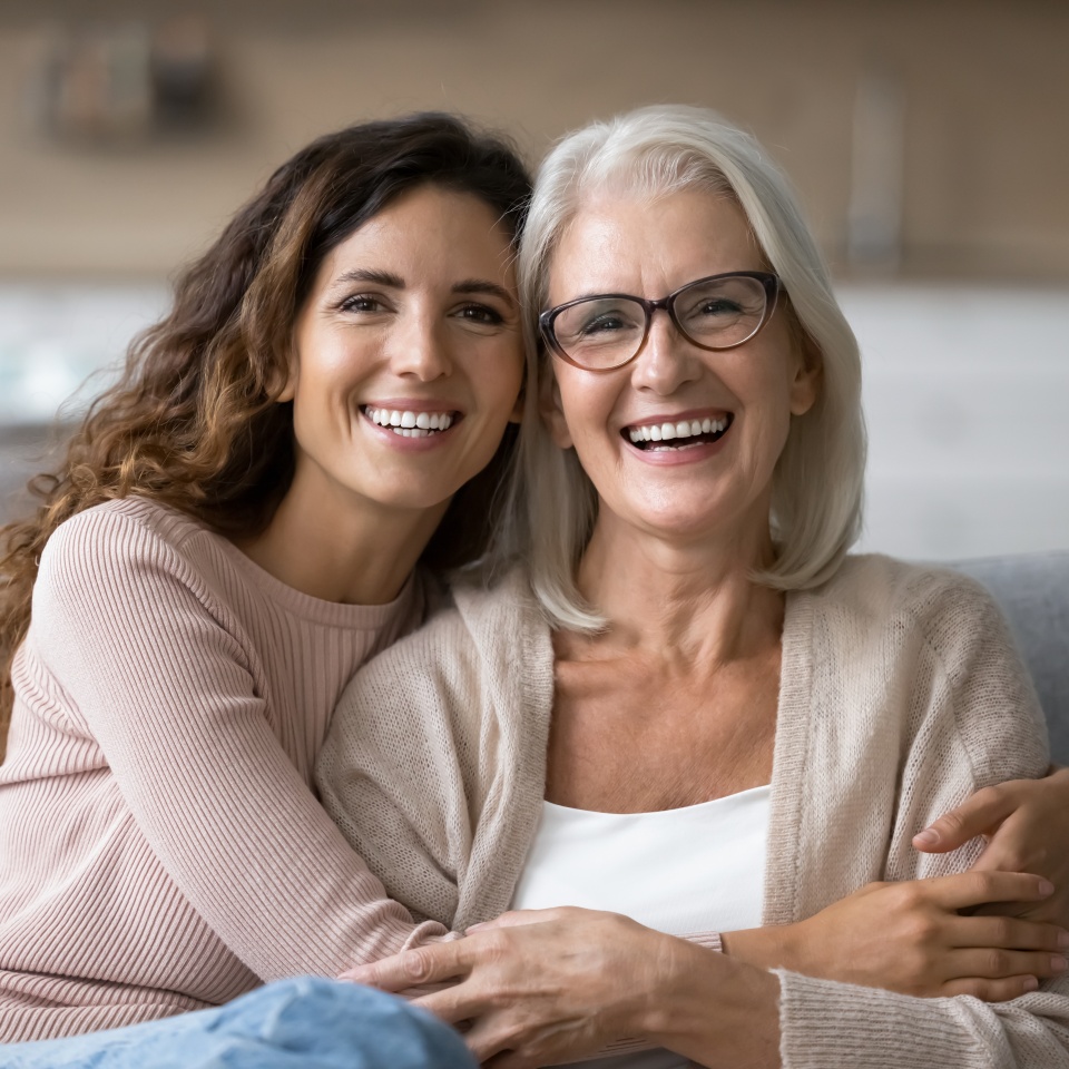 Portrait of two beautiful young and mature females, different generations women hugging sit on sofa, sharing warmth, joyful moments together. Family ties, intergenerational connection, love, support