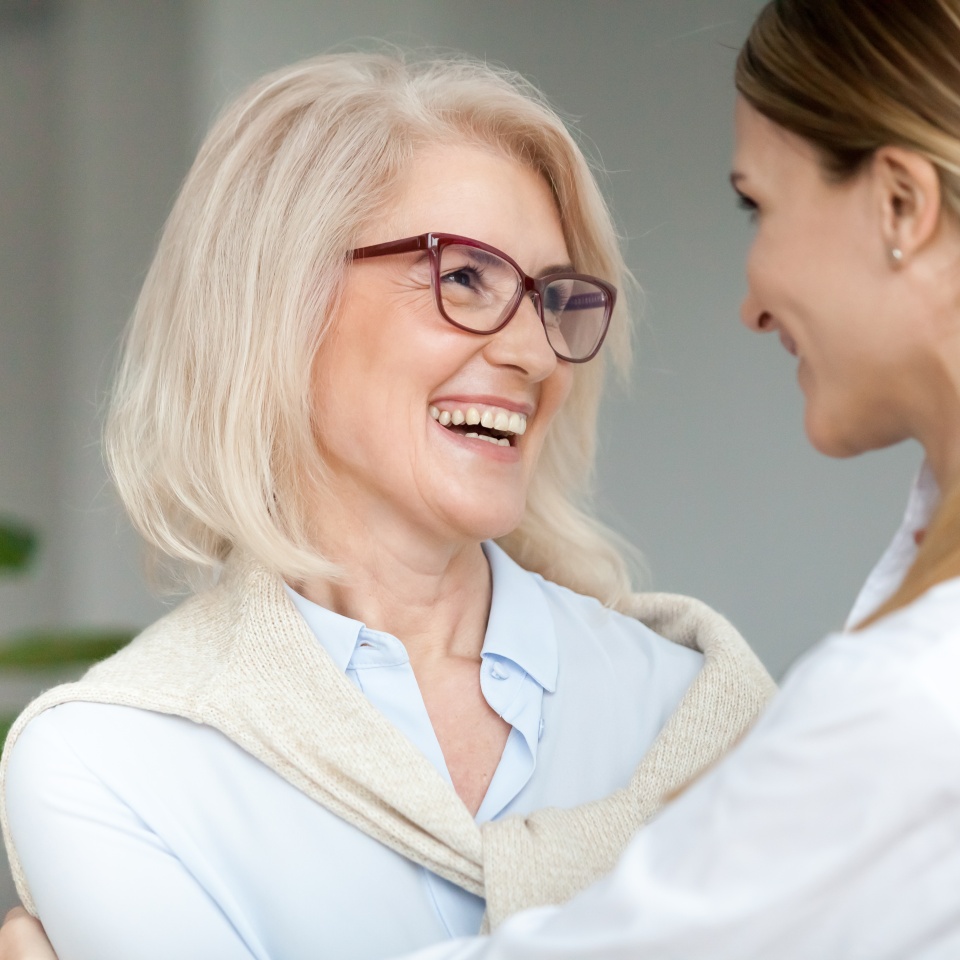 Beautiful aged woman in glasses embracing young adult lady and laughing, smiling attractive senior older mother happy to hug grown-up daughter, warm sincere family bonding having fun together